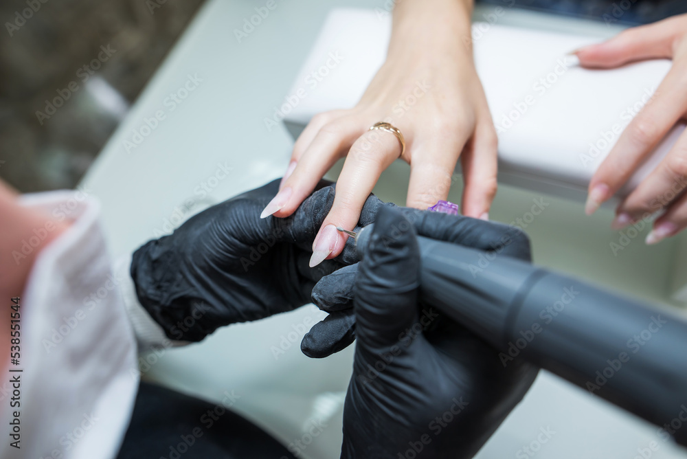 Manicurist makes a manicure to a client girl in a beauty salon.