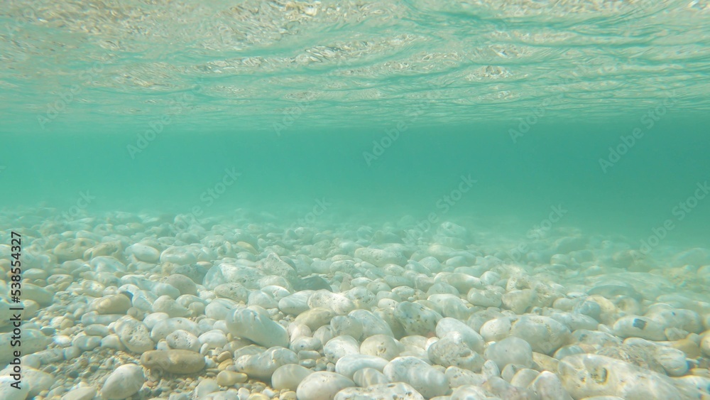 Small stones under clear blue water. Rocky bottom. Pebble shore.