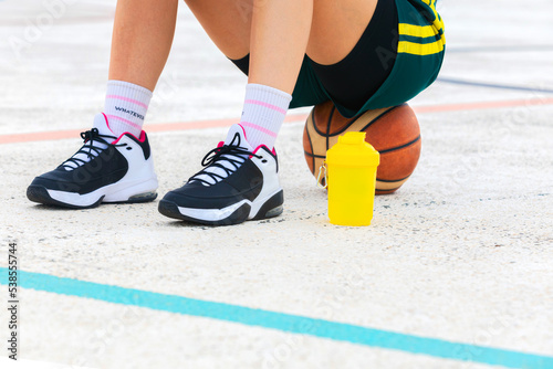 Close-up horizontal detail of the legs and shoes of a female basketball player sitting on a ball. photo