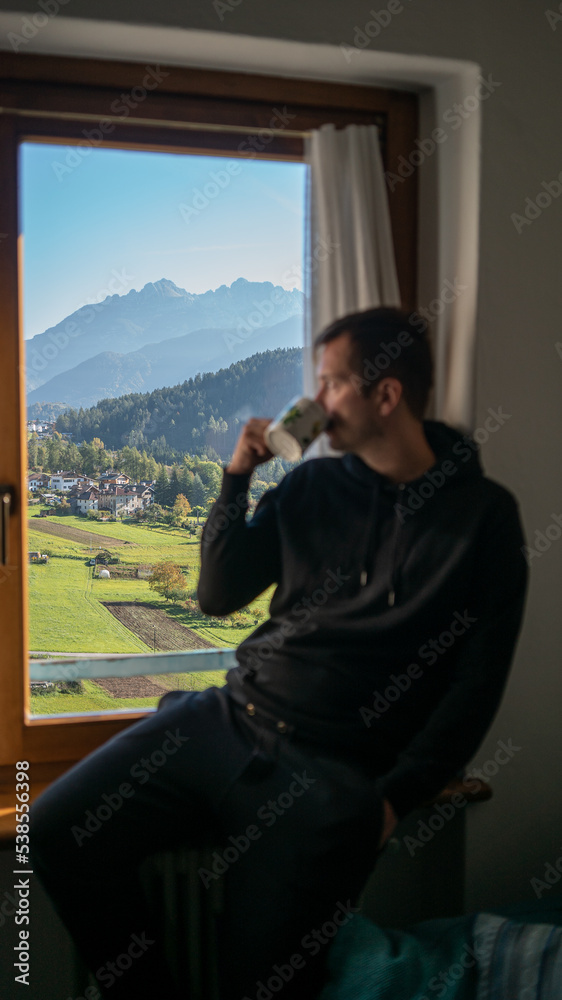 young guy is having morning coffee next to the window in Dolomites young guy is having morning coffee next to the window in Dolomites