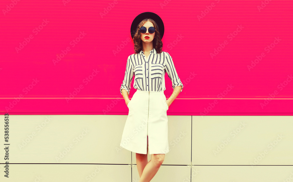 Beautiful young woman model wearing white striped shirt, black round hat, skirt on pink background Beautiful young woman model wearing white striped shirt, black round hat, skirt on pink background