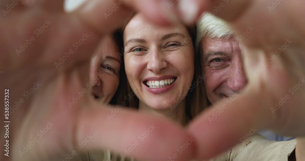 Close up young adult daughter express love and care to older parents, showing to camera heart symbol with joined fingers, celebrate Happy Family Day, multi-generational relatives, bond, unity concept