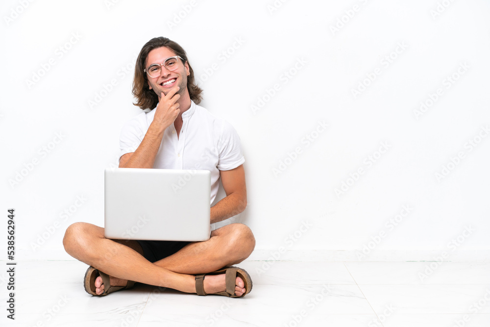 Young handsome man with a laptop sitting on the floor isolated on white background with glasses and smiling Young handsome man with a laptop sitting on the floor isolated on white background with glasses and smiling