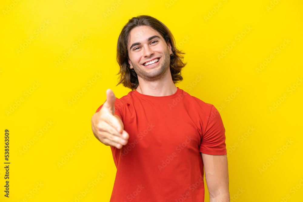 Caucasian handsome man isolated on yellow background shaking hands for closing a good deal Caucasian handsome man isolated on yellow background shaking hands for closing a good deal