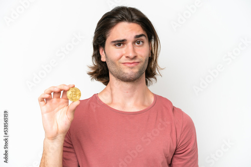 Young handsome man holding a Bitcoin isolated on white background with sad expression © luismolinero