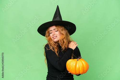 Young caucasian woman costume as witch holding a pumpkin isolated on green screen chroma key background suffering from pain in shoulder for having made an effort
