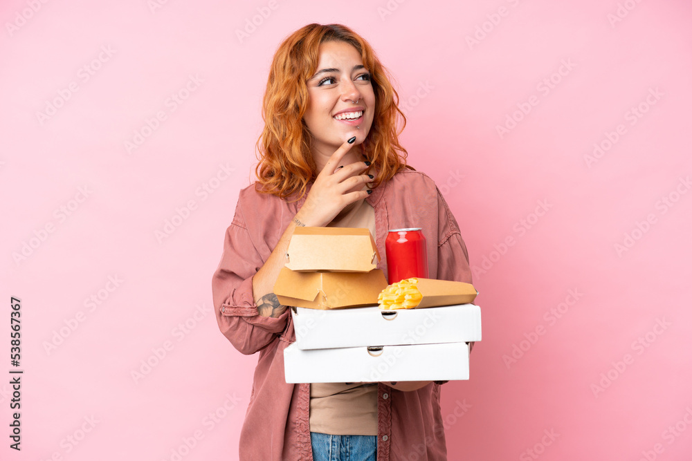 Young caucasian woman holding fast food isolated on pink background looking up while smiling Young caucasian woman holding fast food isolated on pink background looking up while smiling