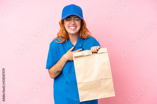 Young caucasian woman taking a bag of takeaway food isolated on pink background smiling a lot