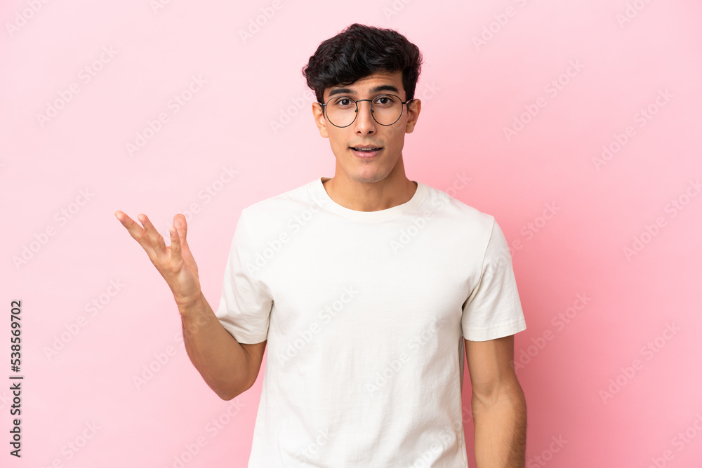 Young Argentinian man isolated on pink background making doubts gesture