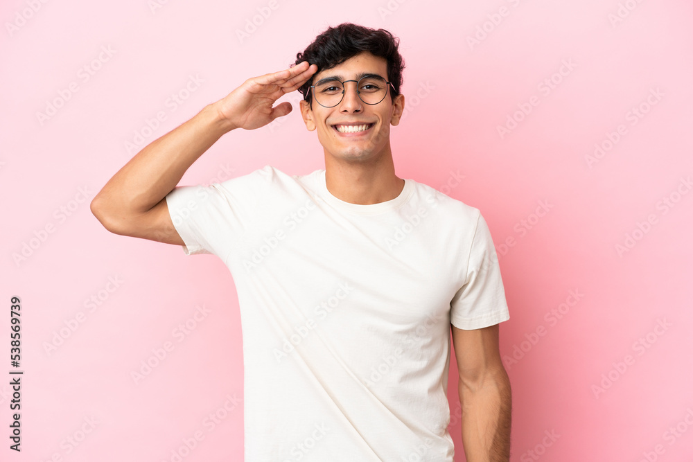 Young Argentinian man isolated on pink background saluting with hand with happy expression Young Argentinian man isolated on pink background saluting with hand with happy expression