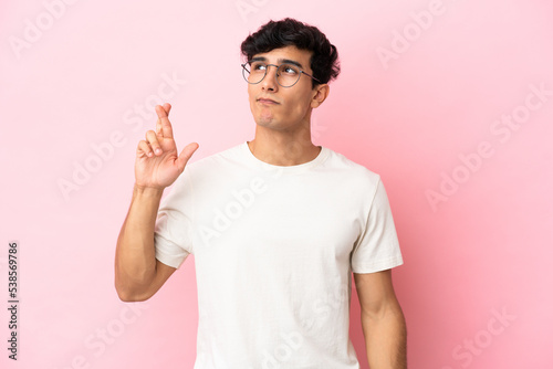 Young Argentinian man isolated on pink background with fingers crossing and wishing the best