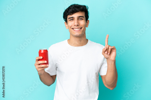 Young Argentinian man holding a refreshment isolated on blue background pointing up a great idea