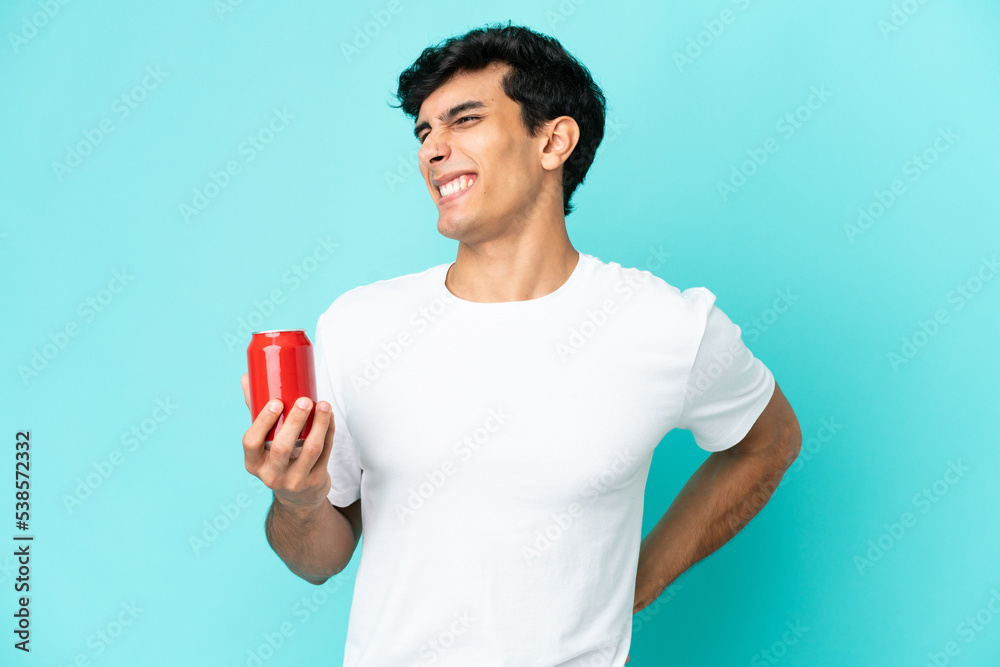Young Argentinian man holding a refreshment isolated on blue background suffering from backache for having made an effort Young Argentinian man holding a refreshment isolated on blue background suffering from backache for having made an effort