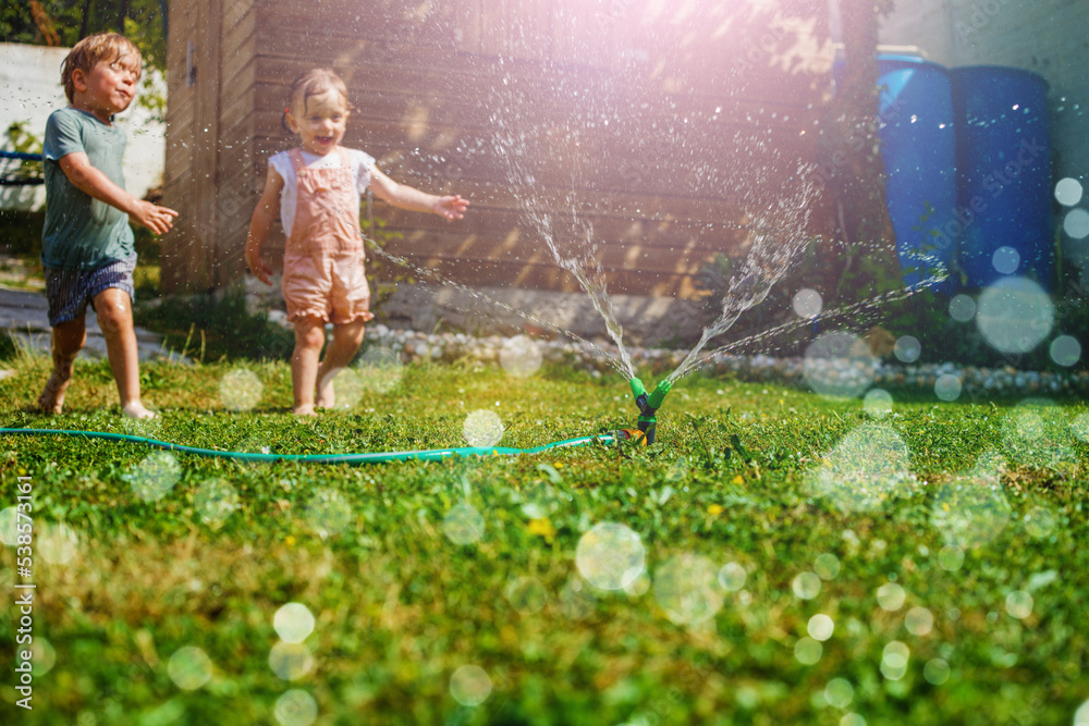 Two children have fun in the garden - playing with water on lawn - obrazy, fototapety, plakaty 