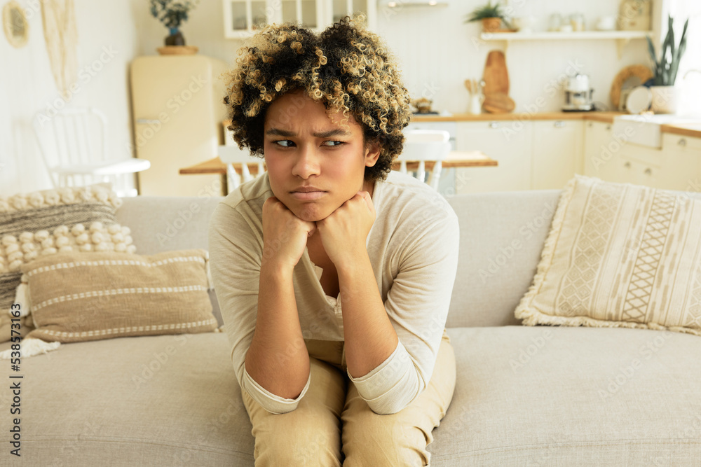 Resentful disappointed frowning millennial african american girl sitting on couch in living-room resting chin on hands, looking away with anger and envy, thinking about unpleasant episode Resentful disappointed frowning millennial african american girl sitting on couch in living-room resting chin on hands, looking away with anger and envy, thinking about unpleasant episode