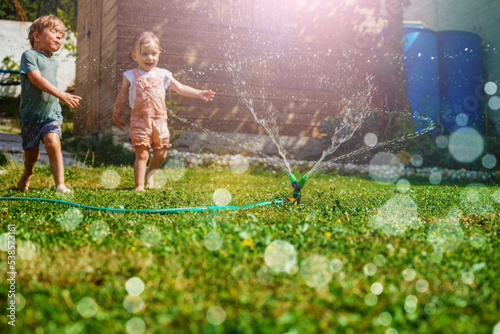 Two children have fun in the garden - playing with water on lawn