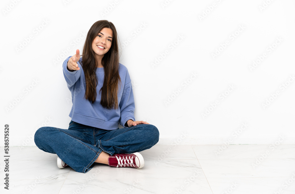 Young woman sitting on the floor shaking hands for closing a good deal Young woman sitting on the floor shaking hands for closing a good deal
