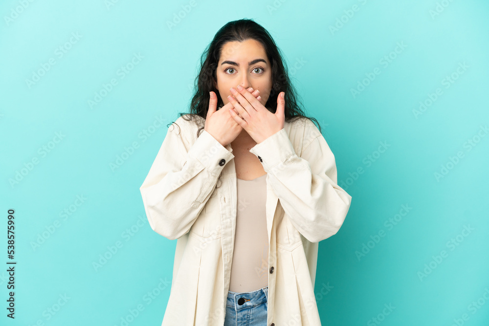 Young caucasian woman isolated on blue background covering mouth with hands