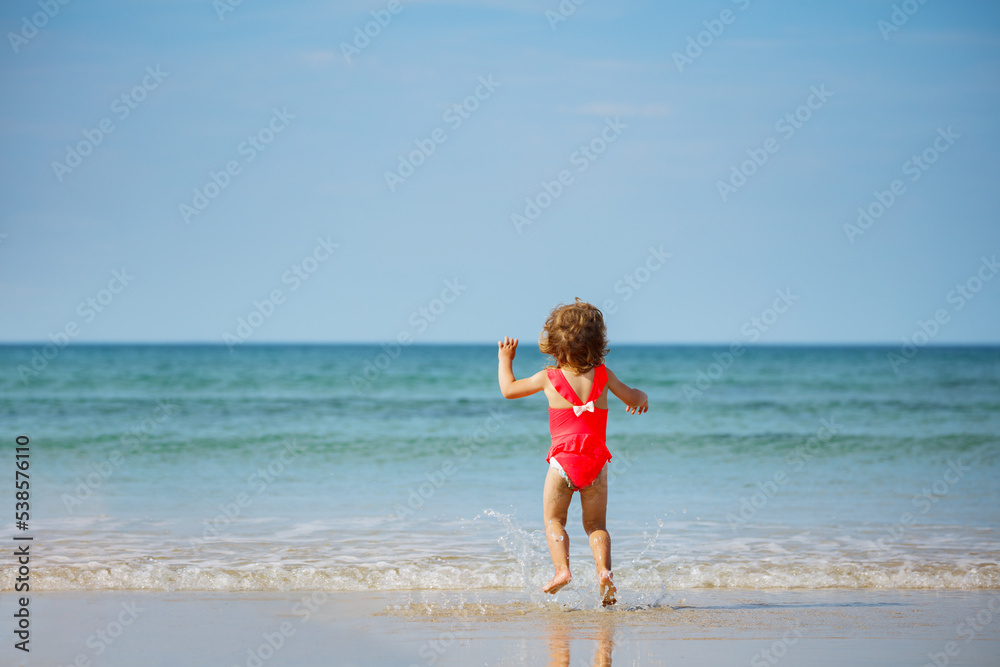 Little cute girl jump in ocean waves on the sand beach