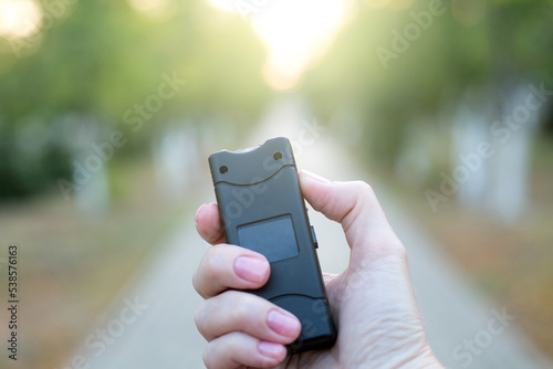 A woman's hand holds a taser in the evening in the park. photo