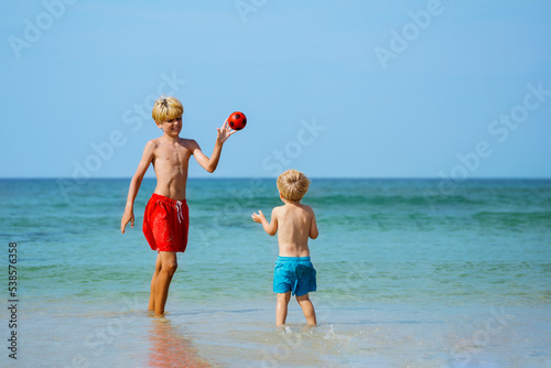 Two happy little boys play with the ball standing in sea