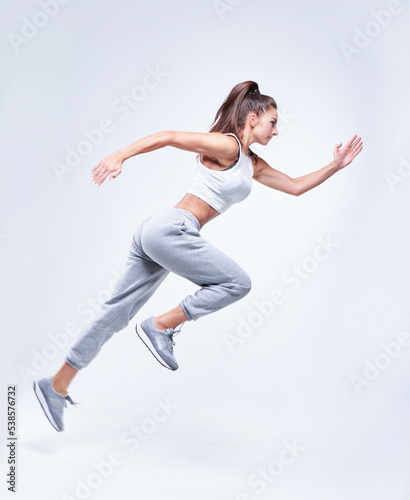Sports woman runner on a white background. Photo of an attractive woman in fashionable sportswear. Dynamic movement. Side view. Sports and healthy lifestyle
