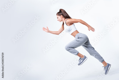 Sports woman runner on a white background. Photo of an attractive woman in fashionable sportswear. Dynamic movement. Side view. Sports and healthy lifestyle