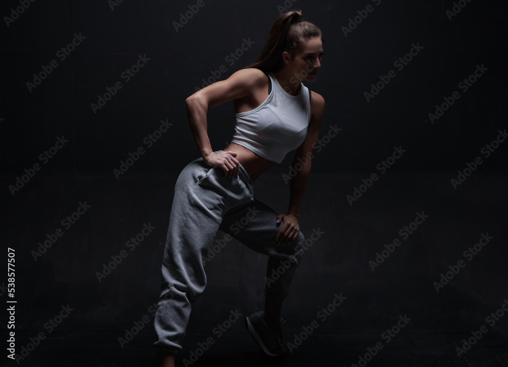 Athletic fitness woman posing in the studio on a dark background. Photo of an attractive woman in fashionable sportswear. Sports and healthy lifestyle Athletic fitness woman posing in the studio on a dark background. Photo of an attractive woman in fashionable sportswear. Sports and healthy lifestyle