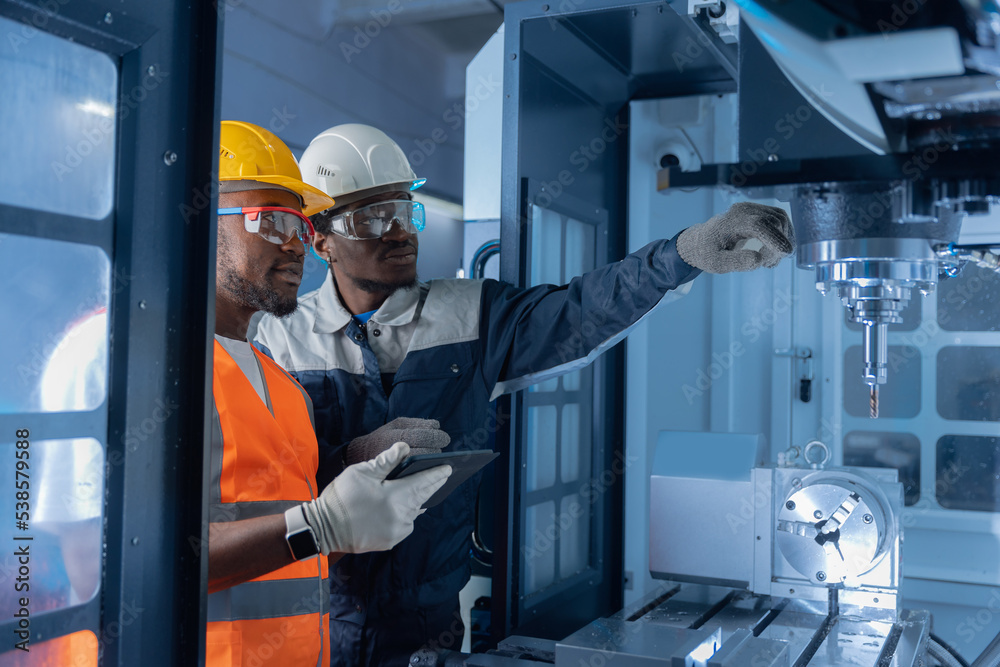 Team african american engineer in uniform using tablet computer for control CNC machinery on industry car factory Team african american engineer in uniform using tablet computer for control CNC machinery on industry car factory