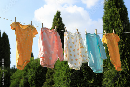 Clean baby onesies hanging on washing line in garden. Drying clothes