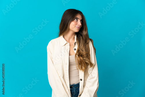 Young caucasian woman isolated on blue background having doubts while looking side