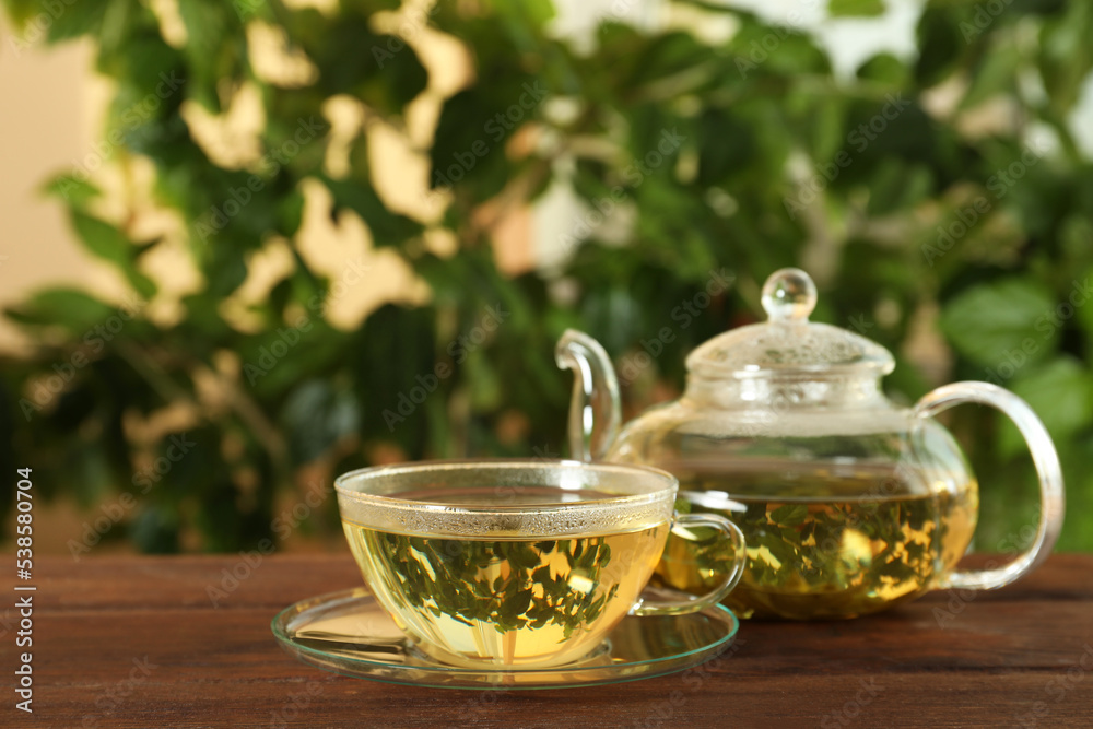 Fresh green tea in glass cup and teapot on wooden table Fresh green tea in glass cup and teapot on wooden table