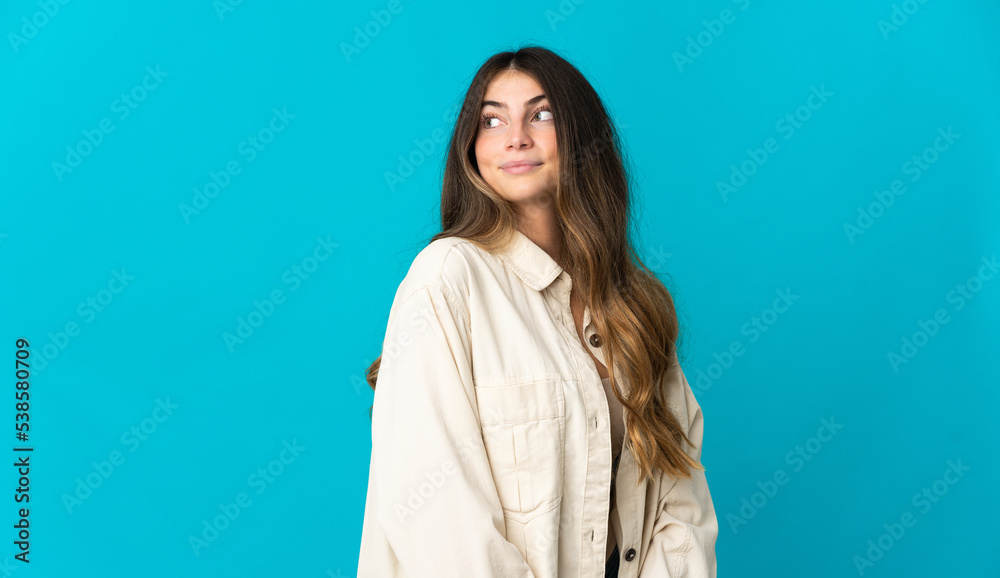 Young caucasian woman isolated on blue background making doubts gesture looking side Young caucasian woman isolated on blue background making doubts gesture looking side