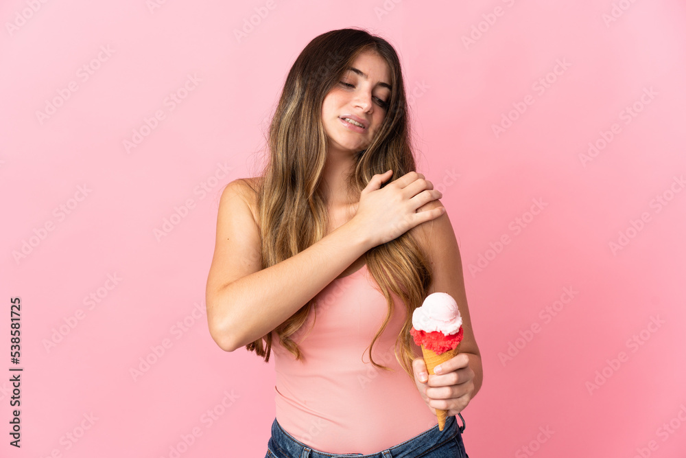 Young caucasian woman with a cornet ice cream isolated on pink background suffering from pain in shoulder for having made an effort Young caucasian woman with a cornet ice cream isolated on pink background suffering from pain in shoulder for having made an effort