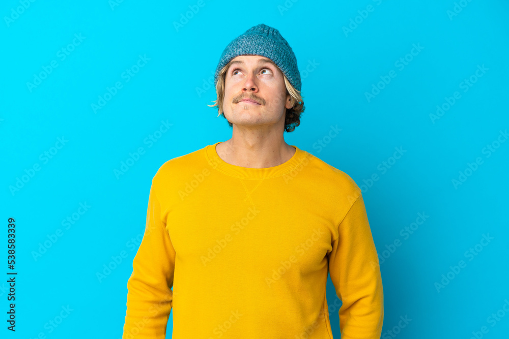 Handsome blonde man isolated on blue background having doubts while looking up Handsome blonde man isolated on blue background having doubts while looking up