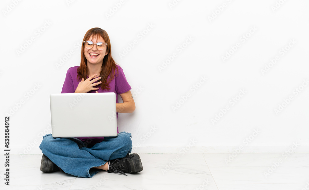 redhead girl with a laptop sitting on the floor smiling a lot