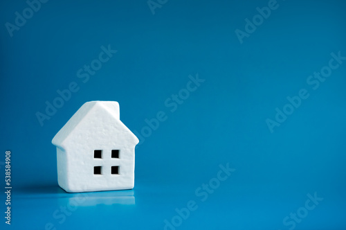 A simple miniature ceramic white house model on blue background with copy space, minimal style. Concepts of residential or real estate property, land and building business and family life.
