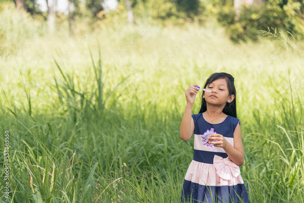 Adorable happy cute girl playful foam bubbles in green playground in summer outdoors. Funny Cheerful girl in the park with happy times.