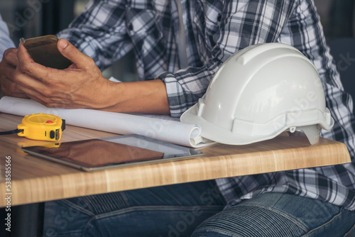 Asian engineer man brainstorming construction building contractor civil worker parners team meeting at constrcution site. Blueprint engineer hardhat worker helmet on table. Engineer teamwork consult photo