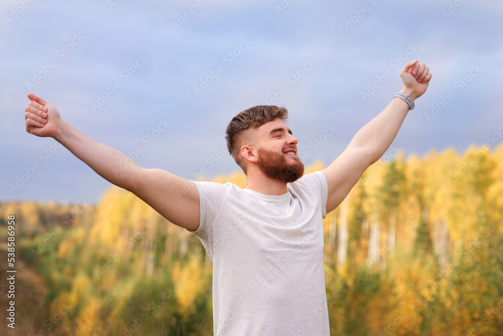 young bearded relaxed calm man enjoying good weather in the forest, park, breathing deep fresh air and smiling. Guy with beard holding his arms hands up behind head, stratching with his eyes closed young bearded relaxed calm man enjoying good weather in the forest, park, breathing deep fresh air and smiling. Guy with beard holding his arms hands up behind head, stratching with his eyes closed