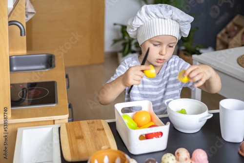 Mother and cute baby boy cooking food at childish kitchen playing chef educational playthings