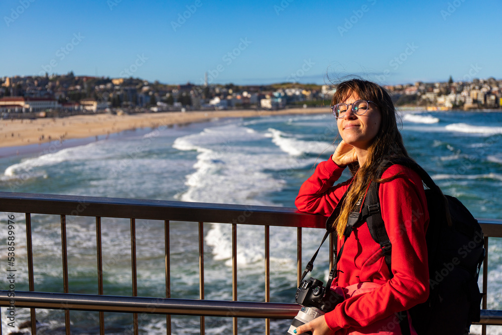 long-haired girl with camera enjoys the setting sun on bondi beach in syndey; famous surfers' beach in sydney long-haired girl with camera enjoys the setting sun on bondi beach in syndey; famous surfers' beach in sydney
