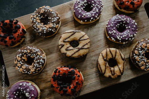 conjunto de donuts de diferentes colores con chocolate y azúcar encima de una tabla de madera