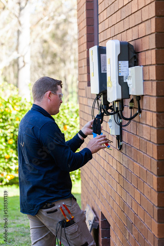 Tradie working as an electrician wiring a solar power control box beside house
