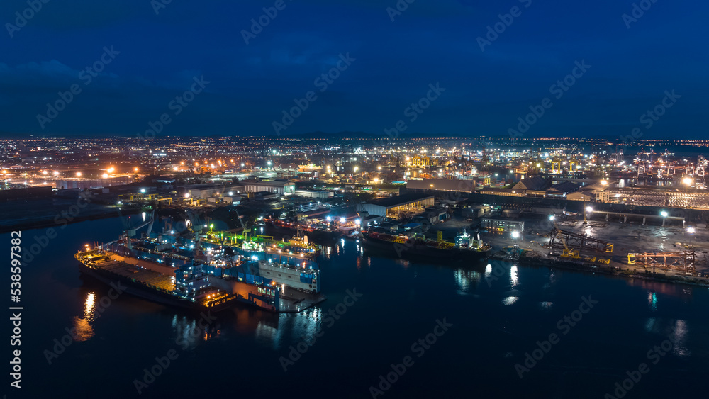 aerial view shipyard dry dock maintenance and repair container ship transport and oil ships in sea, business and industry service at night over lighting cityscape blue sky background
