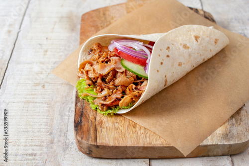 doner donair kebab wrap with spicy meat, lettuce, tomato, red onion. Served on wooden cutting board. Copy space for text or logos.