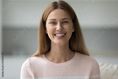 Head shot of happy beautiful woman sits on sofa staring at camera pose alone at modern home. Portrait of satisfied young 35s tenant or female homeowner or housewife spend time in own or rented flat photo