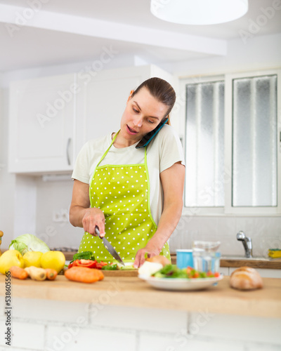 Young woman talking on phone while cooking dinner at home