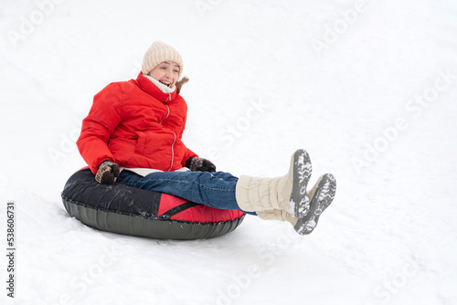 Young woman in red jacket rides inflatable sled down slide. Girl laughs and has fun outside in winter weather photo