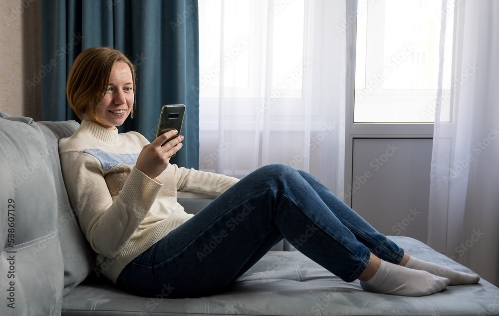 Beautiful smiling girl relaxing on a couch and using mobile phone Beautiful smiling girl relaxing on a couch and using mobile phone
